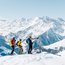 Drei Wanderer auf schneebedecktem Gipfel mit Alpen im Hintergrund