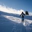 Skifahrer steigt mit Stöcken einen schneebedeckten Hang hinauf bei sonnigem Himmel