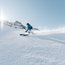 Skifahrer fährt bei Sonnenschein auf verschneiter Piste in den Bergen